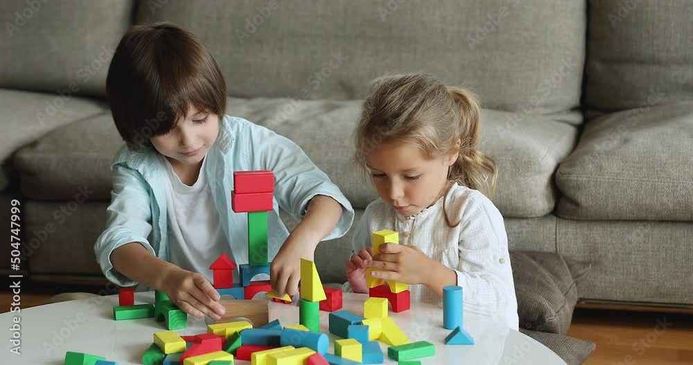 Two cute little kids play wooden cubes. Preschool siblings sit at table in modern living room use multi colored bricks enjoy playtime look concentrated while construct together. Games at home concept Two cute little kids play wooden cubes. Preschool siblings sit at table in modern living room use multi colored bricks enjoy playtime look concentrated while construct together. Games at home concept