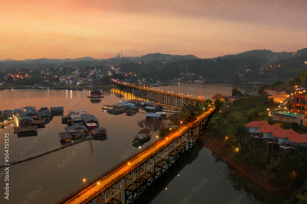 Aerial top view of Mon Bridge with residential local houses in Mon village, nature trees, Sangkhlaburi, Kanchanaburi, Thailand in urban city town in Asia, buildings.