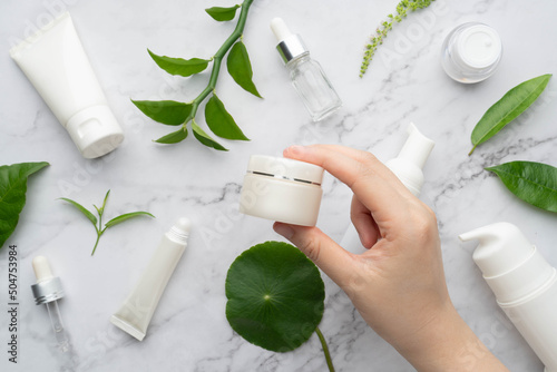 Young female hand holding facial moisturizer cream bottle with organic natural skincare products on marble background. Beauty cosmetic skincare and cosmetology concept. photo