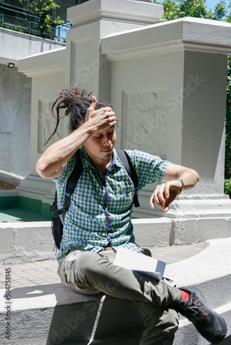 Young man with dreadlocks looking at the time on his wristwatch, surprised by the lateness of the hour