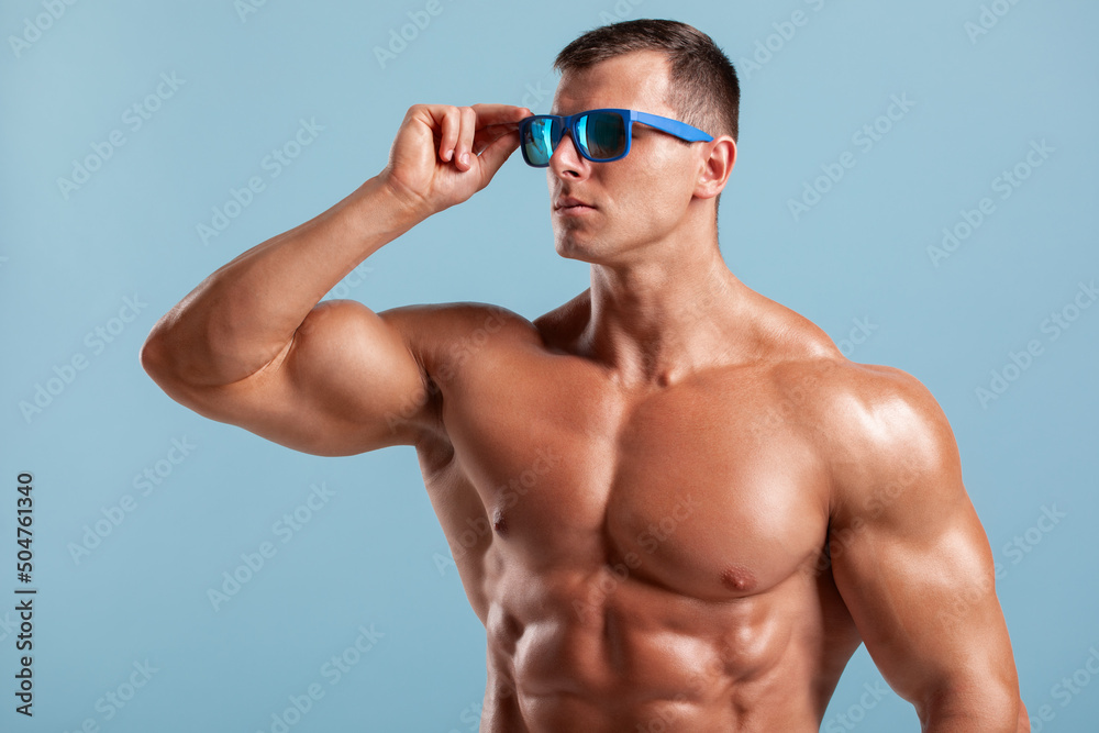 Handsome muscular man in sunglasses, naked torso abs. Fitness male model on blue background