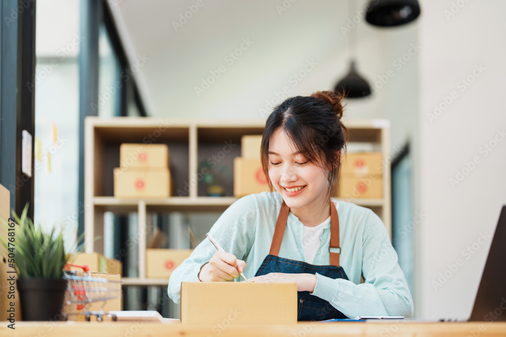 A portrait of a small startup, and SME owner, an Asian female entrepreneur, is writing down information on a notepad to organize the product before packing it into the inner box for the customer A portrait of a small startup, and SME owner, an Asian female entrepreneur, is writing down information on a notepad to organize the product before packing it into the inner box for the customer