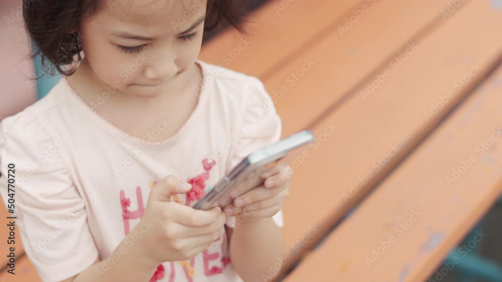 Close up face of adorable asian girl who is using smartphone alone at school which is digital lifestyle of the kid to use technology for her communication, learning and entertainment with happiness. Close up face of adorable asian girl who is using smartphone alone at school which is digital lifestyle of the kid to use technology for her communication, learning and entertainment with happiness.
