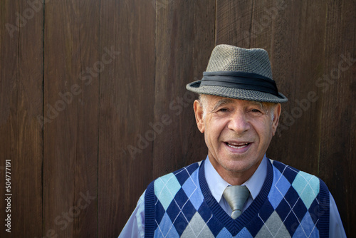 фотографія caucasian male senior adult with a fedora hat, blue vest and a brown wooded plan