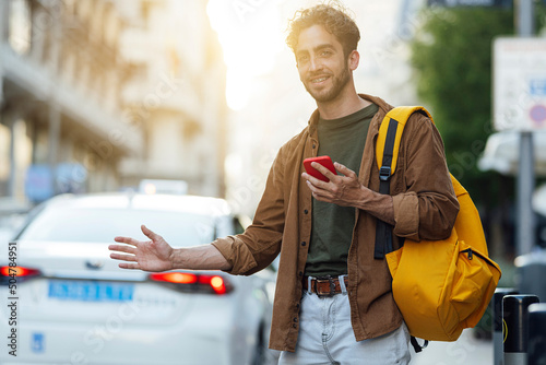 Outdoor portrait of handsome young hipster man with mobile phone waiting for taxi.
