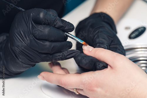 Manicurist paints nails with gel polish. Applying acrylic nail lacquer. Manicure service. The specialist covers the client's nail with a transparent gel.