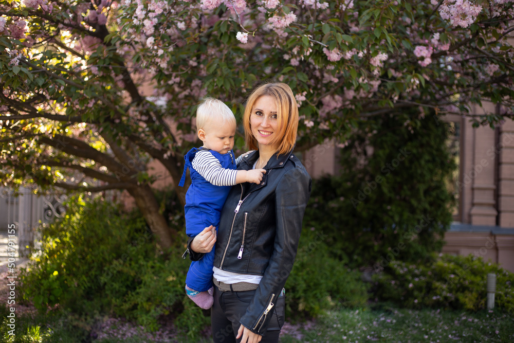 Fototapeta premium mother and little boy son having fun in spring park near pink sakura blooming tree. Spring concept