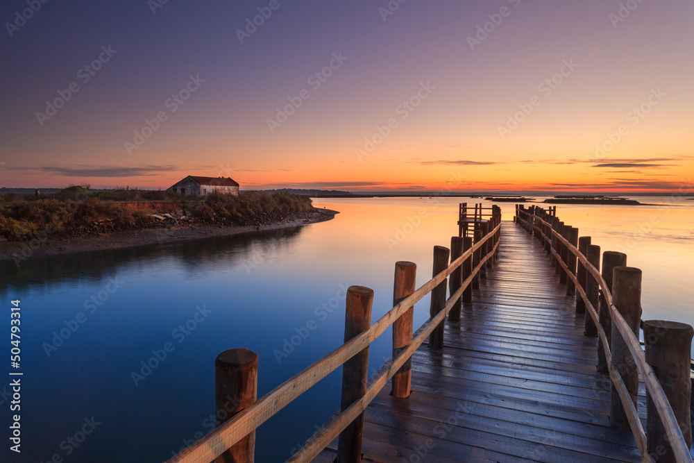 Amazing romantic view from the pier at sunset. Serene landscape on the lake at colorful sunset. Old wooden pier in a fineart photo