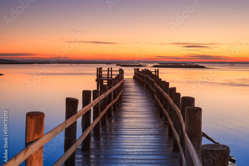 Amazing romantic view from the pier at sunset. Serene landscape on the lake at colorful sunset. Old wooden pier in a fineart photo