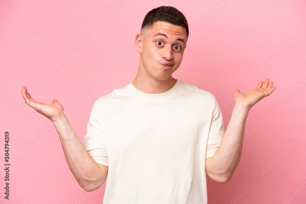 Young Brazilian man isolated on pink background having doubts while raising hands Young Brazilian man isolated on pink background having doubts while raising hands