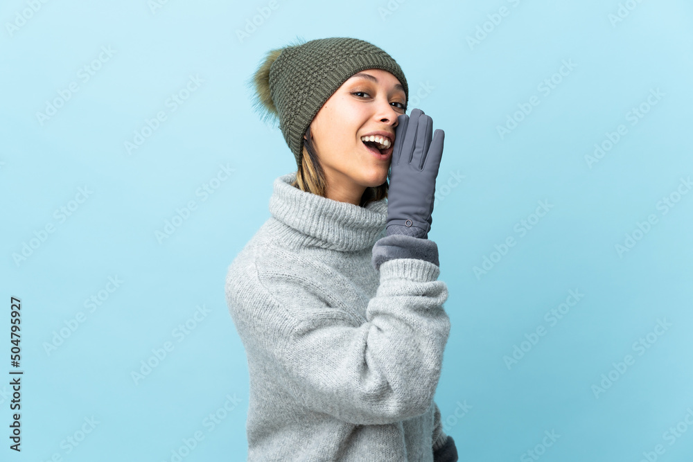 Young Uruguayan girl with winter hat isolated on blue background whispering something Young Uruguayan girl with winter hat isolated on blue background whispering something