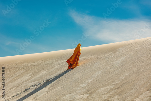 Canvas woman in yellow arabic clothing climbing a dune in the desert