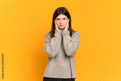 Young Ukrainian girl isolated on yellow background frustrated and covering ears © luismolinero