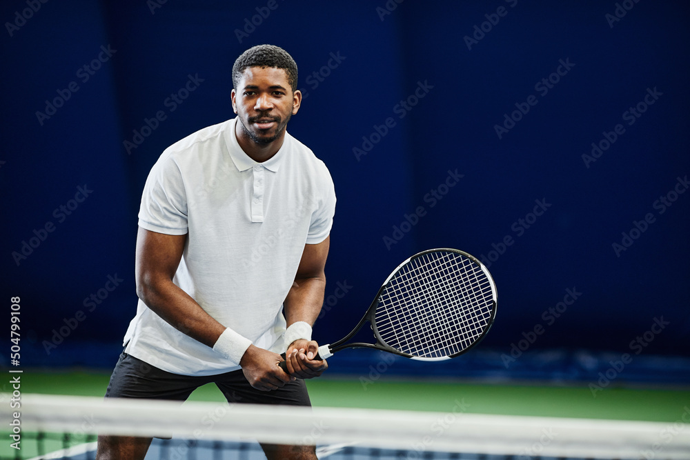 Front view portrait of handsome black sportsman playing tennis at indoor court, copy space
