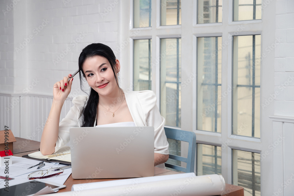 Charming young Asian female architect holding a pencil while thinking about her project at home office. Charming young Asian female architect holding a pencil while thinking about her project at home office.