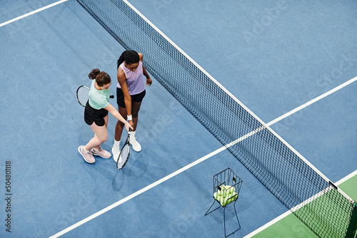 Minimal top view of female tennis coach working with client against blue court floor, copy space