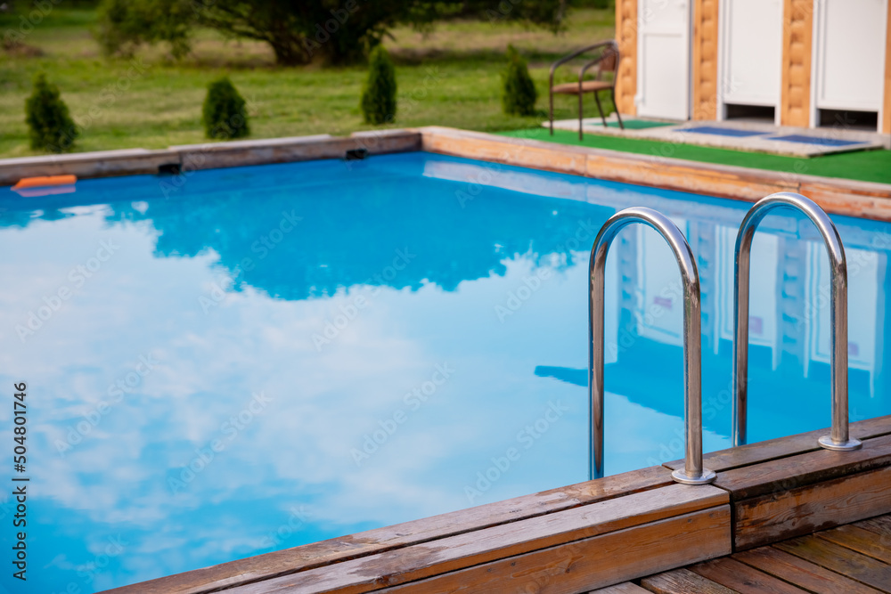 Ladder stainless handrails for descent into swimming pool.Metal Handrails and blue water at sunset. Swimming and summer rest concept.pool with stair and wooden deck.copy space