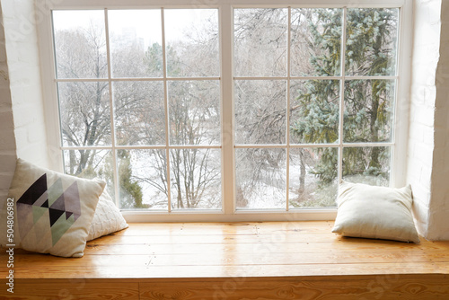 Сozy and frost winter still life, white pillows on windowsill against snow landscape from outside photo