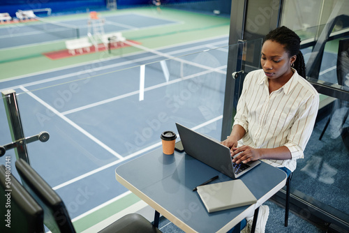 Fototapeta Naklejka Na Ścianę i Meble -  High angle portrait of young black businesswoman using laptop while working in sports training center