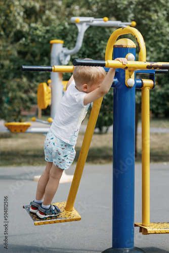 Fototapet The little boy swings and perform exercises on an outdoor gym equipment