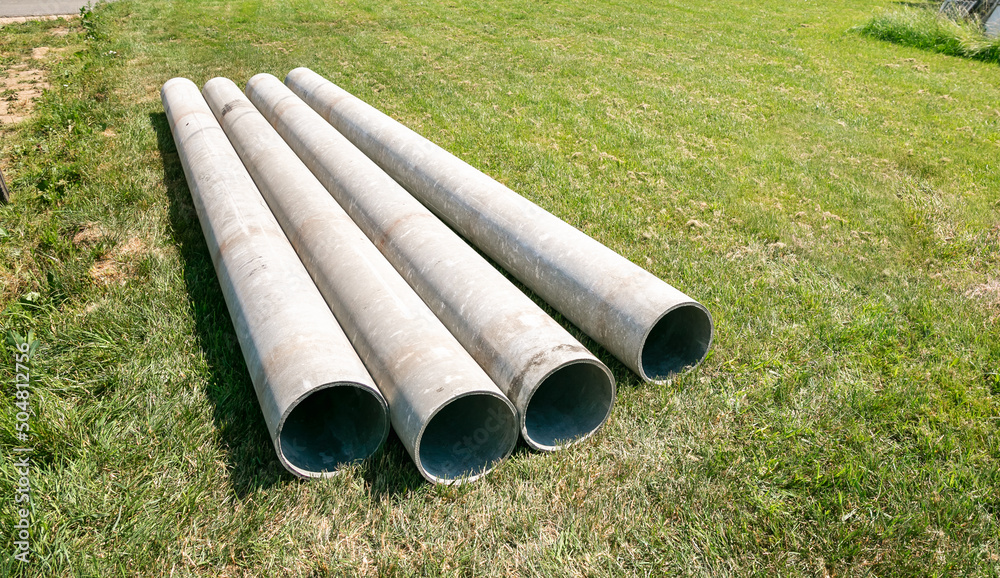 Chrysotile cement pipes lie on the green grass of construction site. Four round tubes. Copy space. Building element. Column concept. Drainage material. Large sewerage culvert. Industrial engineering