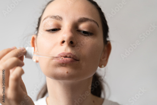 Portrait of dark haired young woman taking oil supplement with glass dropper. CBD hemp medicine oil applying on the tongue 