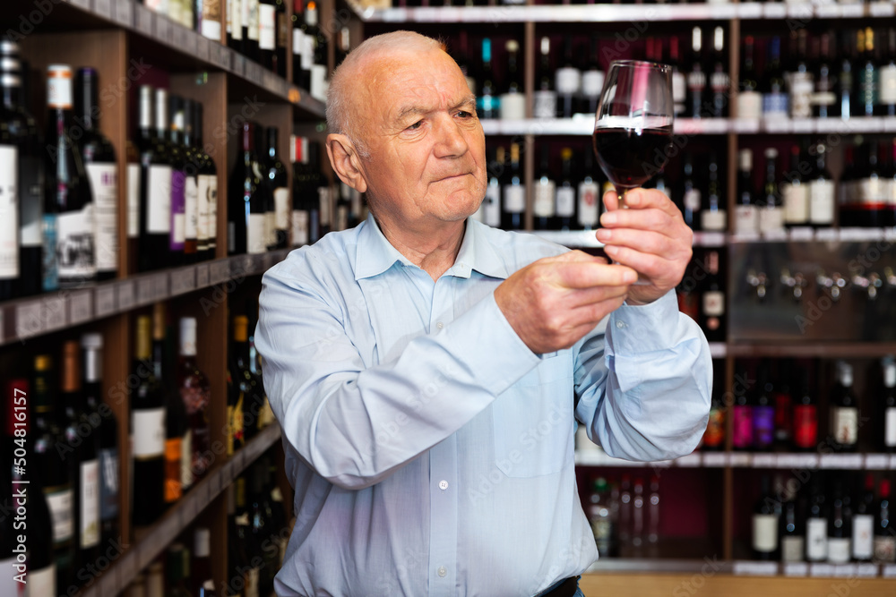 portrait of senior man checks the color and taste of red wine in a liquor store