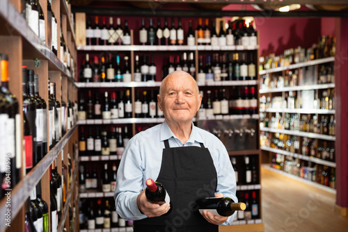 Happy positive senior male vintner giving recommendation about purchase wine in his wine house