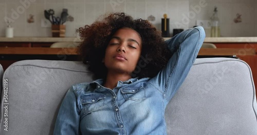 Calm millennial Afro American woman enjoy peaceful rest on sofa nap dream with closed eyes then look aside with smile imagine good future. Happy teenage female relax feel peace of mind relieve stress
