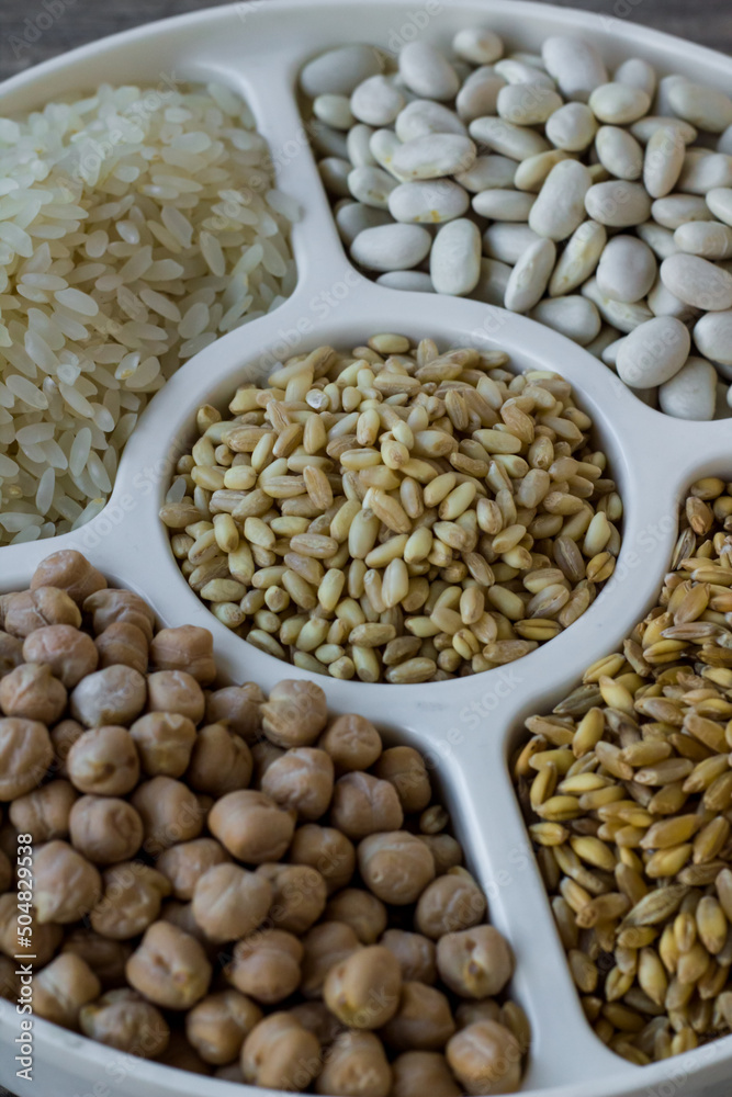 Obraz premium Uncooked dried chickpeas, wheat, rice and white beans in divided plate on wooden surface