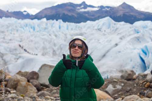 happy girl in a warm jacket and a protective helmet and sunglasses getting ready to go hiking on the Perino Moreno glacier, Argentina, El Calafate