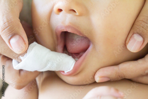 Mother cleans the teeth of a little boy, him to reduce pain from erupting , baby teethfingertip brush for children,  Clean cloth fter bathing at home, Asian family, hygiene. Zoom Selective focus