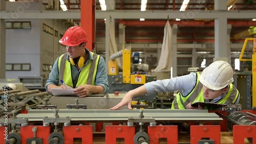 Two young engineers Testing and verifying the operation of the machines forming metal sheet tiles in the factory
