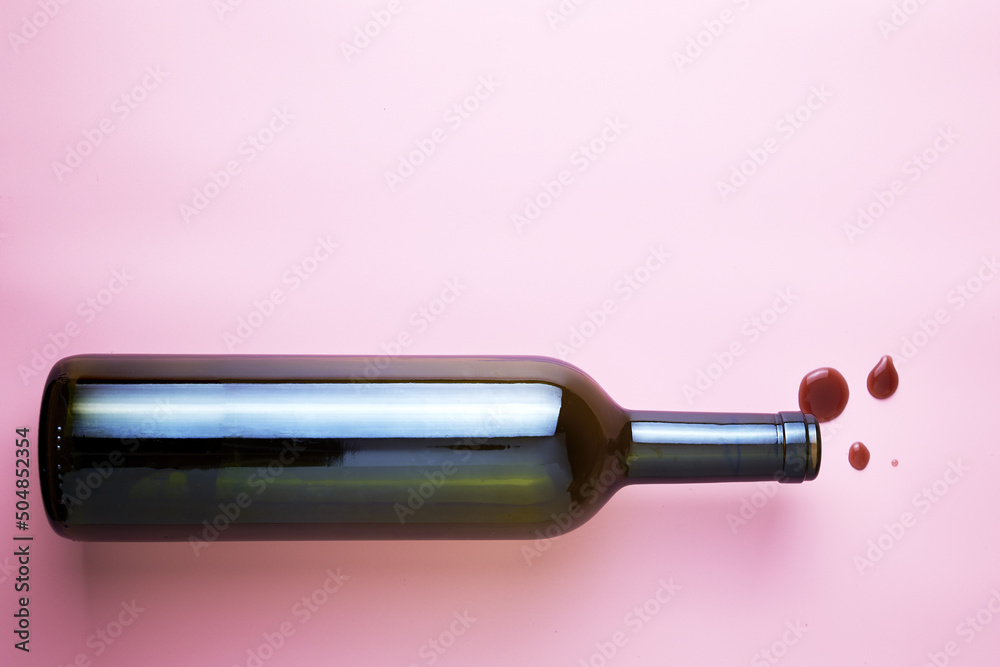 glass wine bottle and drops of red wine on a pink background copyspace glass wine bottle and drops of red wine on a pink background copyspace
