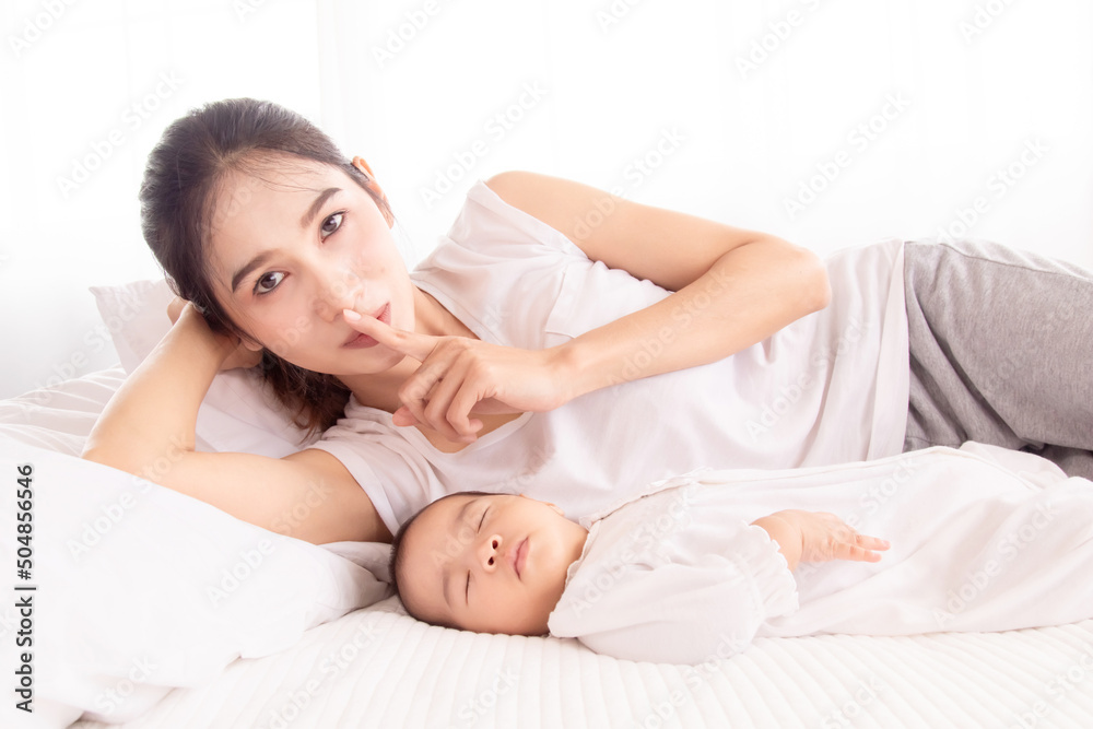 Newborn baby sleeping, Beautiful Asian mother lying next to toddler with love and caring. mom asks not to make noise because the child is sleeping deeply. Newborn baby sleeping, Beautiful Asian mother lying next to toddler with love and caring. mom asks not to make noise because the child is sleeping deeply.
