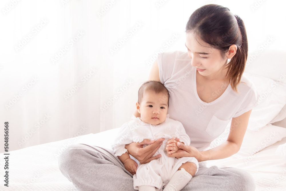 Asian mother holding infant and looking baby with love and tender, mom play with toddler. Beautiful Asian women in white casual t-shirt and newborn in white cotton soft textile. Asian mother holding infant and looking baby with love and tender, mom play with toddler. Beautiful Asian women in white casual t-shirt and newborn in white cotton soft textile.