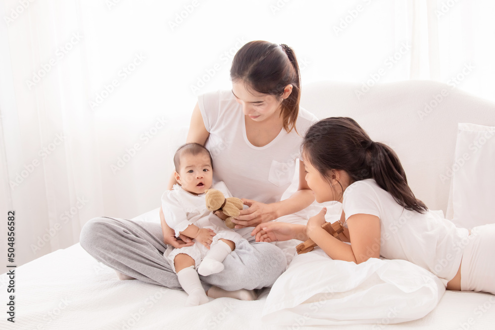 Older asian sister play and talk with newborn on bed in white room, Beautiful mother holding baby adorable and looking with love and caring. happy family concept. Older asian sister play and talk with newborn on bed in white room, Beautiful mother holding baby adorable and looking with love and caring. happy family concept.