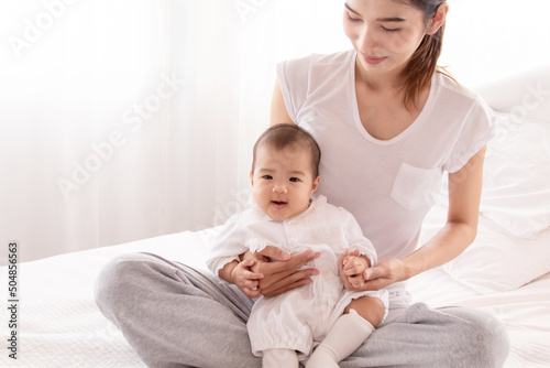 Asian mother holding infant and looking baby with love and tender, mom play with toddler. Beautiful Asian women in white casual t-shirt and newborn in white cotton soft textile. © Rakchanok