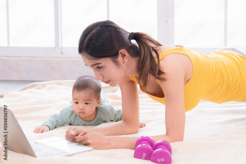 Asian mother workout after delivery newborn baby, young mom watching videos training lose weight yoga sport by computer laptop, beautiful women and toddler infant play together with love and caring Asian mother workout after delivery newborn baby, young mom watching videos training lose weight yoga sport by computer laptop, beautiful women and toddler infant play together with love and caring