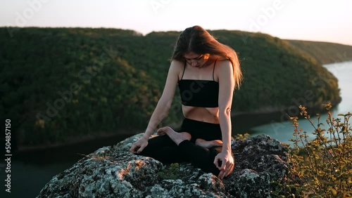 Young woman doing yoga belly exercise - Kapalabhati yogic breathing technique.Yogi does uddiyana bandha, while sitting in lotus pose on high cliff above water outdoors.Lady breathing and meditating photo