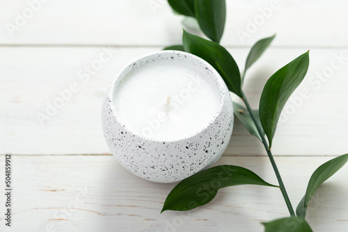 Composition with a candle and a sprig of a plant on a white table. Home interior.