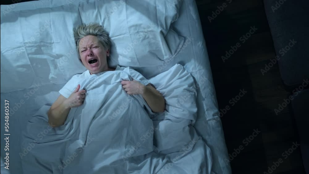 Sleeping man screaming in his sleep in bed, top view. Nighttime panic attacks or nightmares in