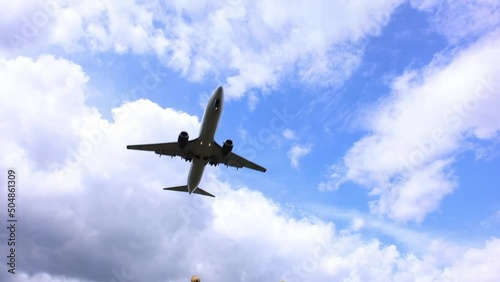 Landing of an airplane flying overhead. In the background there is a beautiful blue sky and fluffy clouds. The plane is preparing to land on the runway on a clear sunny summer day.