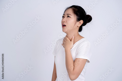 Sore throat woman touches her inflamed throat. Portrait of an Asian woman in a white shirt on a white background. Medical concept. photo