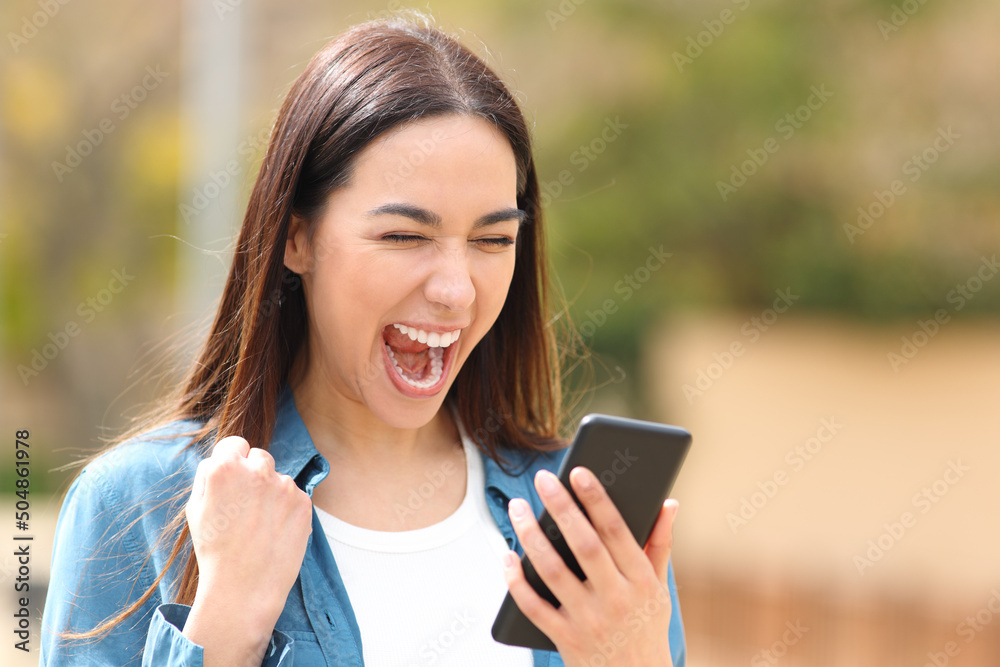 Excited woman checking cell phone in the street Excited woman checking cell phone in the street