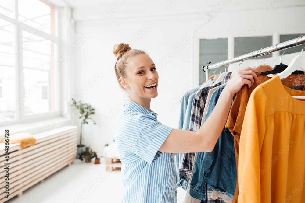 Happy fashion designer hanging clothes on rack in studio Happy fashion designer hanging clothes on rack in studio