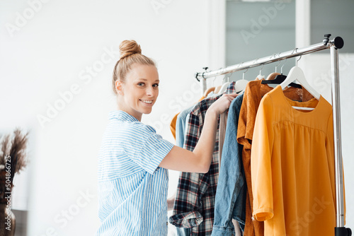 Smiling fashion designer arranging clothes in rack at studio photo