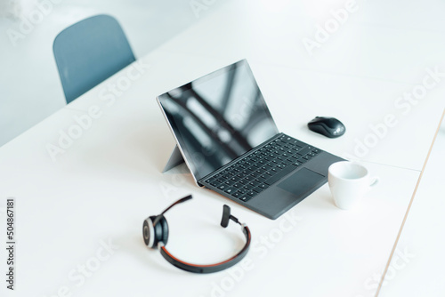 Tablet PC with headset and coffee cup on white desk at office photo