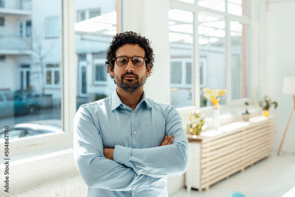 Businessman standing with arms crossed in front of window Businessman standing with arms crossed in front of window