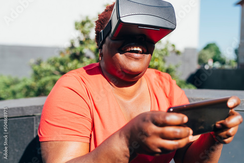 Playful woman wearing virtual reality holding smart phone on sunny day photo